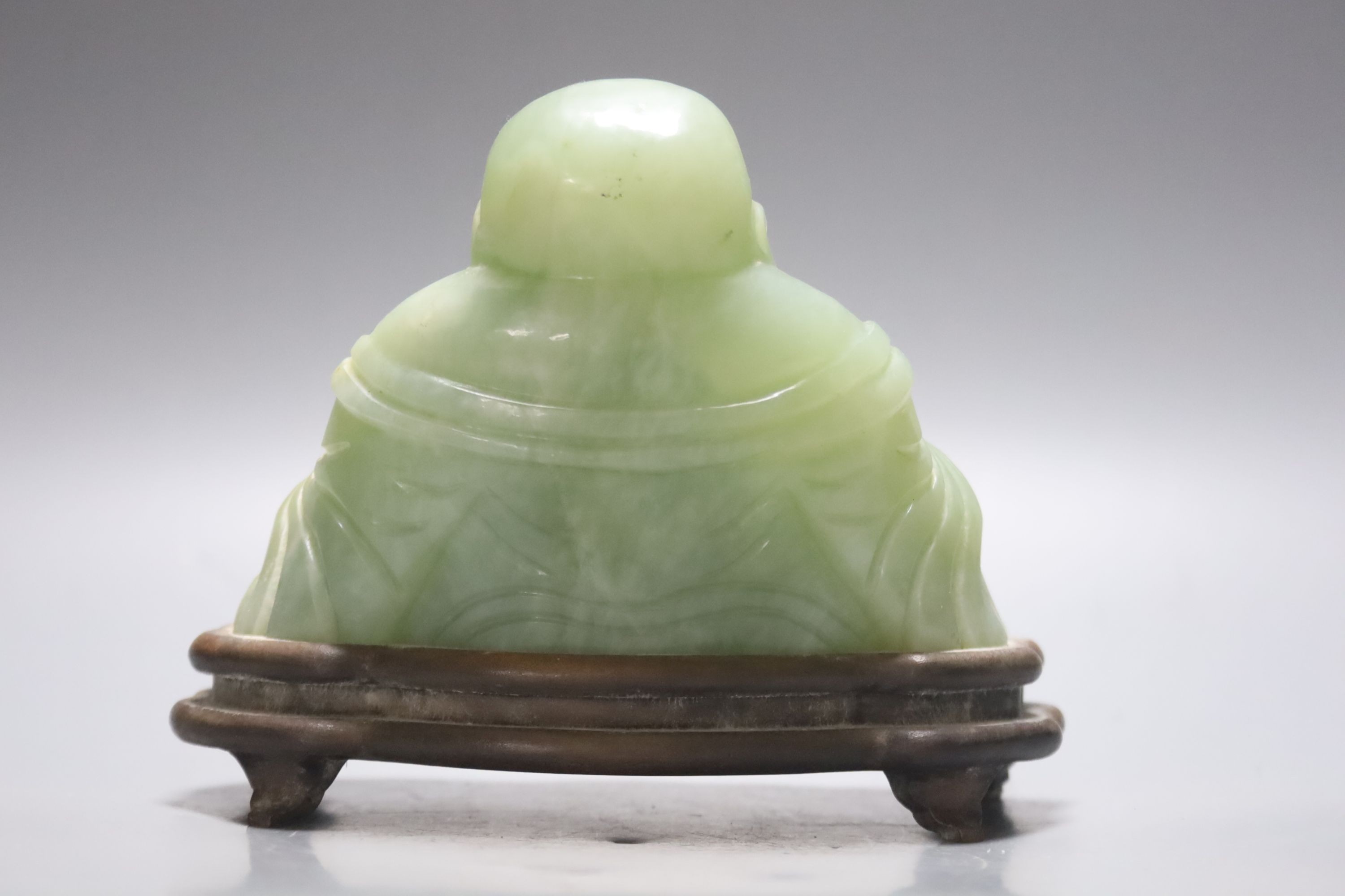 A Chinese carved bowenite jade figure of a seated Budai, H 9cm, W 13cm on carved wooden stand